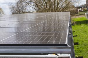 Gros plan sur des panneaux solaires installés sur un toit, avec des arbres et un bâtiment en arrière-plan. L'installation est propre et bien alignée, capturant l'énergie solaire pour une utilisation durable.