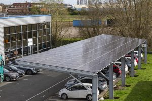 Structure métallique avec panneaux photovoltaïques installés au-dessus d'un parking. Les panneaux solaires fournissent de l'ombre aux voitures stationnées et génèrent de l'énergie renouvelable.